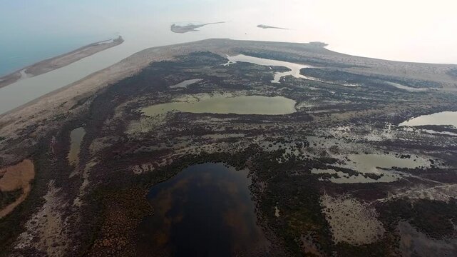 Aerial view of coastal lake lagoon and sandy tombolo spit shaping river mouth plain. Calm shallow waters meet sea sandbar forming natural barrier between open water beside shoreline.