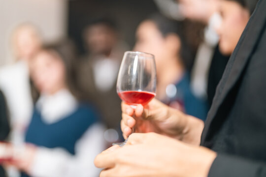 Wine glass red wine hand party social event blurred background adult standing drink celebration beverage stemware glass indoor gathering cocktail tasting luxury elegant close up focus people crowd