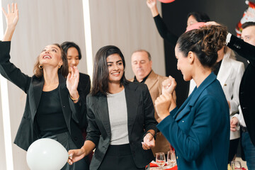 Fototapeta na wymiar Business party celebration with diverse adult worker group dancing and smiling in office interior, joyful social gathering