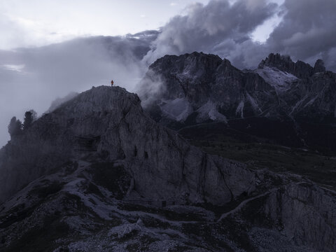 Aerial view of Croda Negra mountain peak with a person in a red jacket standing on a rocky ridge at Passo Falzarego, Veneto, Italy.