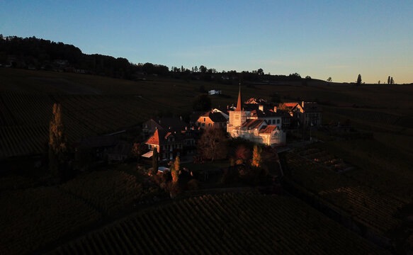 Aerial view of the historic Fechy-Dessus hamlet and its church surrounded by terraced vineyards during sunset in Fechy, Vaud, Switzerland.