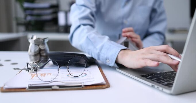 Individual Reviewing Financial Reports.An Asian individual reviews financial reports and property rates, calculating income and expenses with serious dedication using technology.

