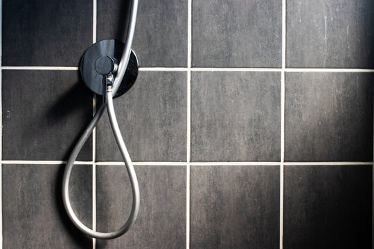 Modern bathroom interior featuring a chrome shower faucet and flexible hose against a dark grey square tiled wall with white grout lines