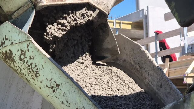 Slow motion close up of wet concrete texture sliding down the metal discharge chute of a mixer truck.