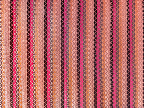 Close up of fabric in repetitive chevron and vertical stripes pattern. Vibrant colorful chevron zigzag pattern in beige, yellow, red, and black color. Seamless background texture.
