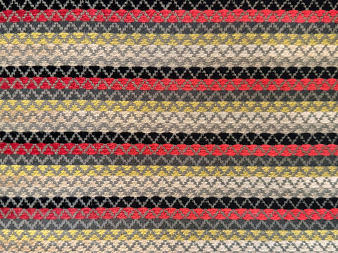 Close up of fabric in repetitive chevron and horizontal stripes pattern. Vibrant colorful  chevron zigzag pattern in beige, yellow, red, and black color. Seamless background texture.