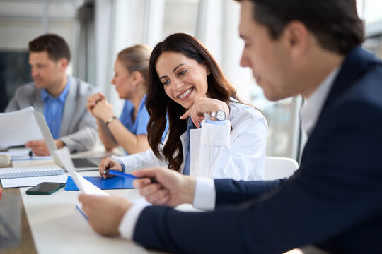 Young female doctor cooperating with an entrepreneur while going through paperwork during a meeting with their colleagues in the office