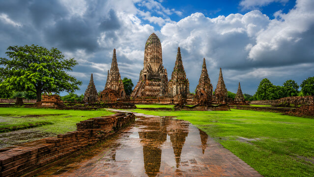 Ancient Buddhist temple ruins with dramatic sky reflection in rain puddle at historic site in Thailand
