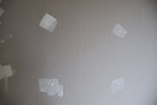 Close-up of a grey drywall surface with distinct white spackle patches covering screw holes and minor damage, ready for sanding and painting