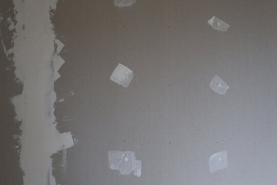 Grey plasterboard wall showing ongoing repair work with a large vertical area of joint compound on the left and smaller filled holes scattered across the surface