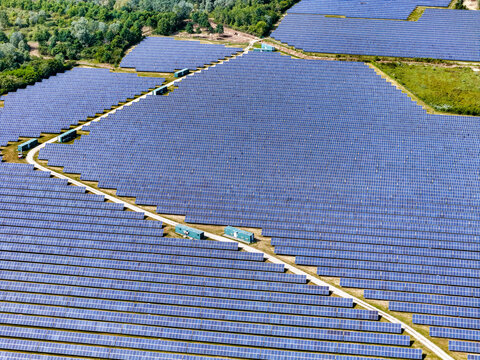 Aerial view of a large solar panel farm with rows of blue photovoltaic modules and green containers surrounded by lush forest in Torrazza Piemonte, Piemonte, Italy.