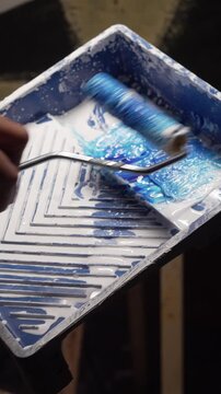 applying white paint with a roller next from paint tray in studio setting.