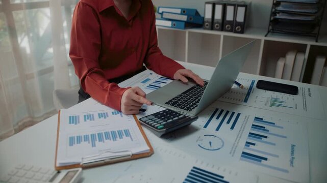 Financial analyst using a calculator and laptop to analyze business data and corporate reports at an office desk