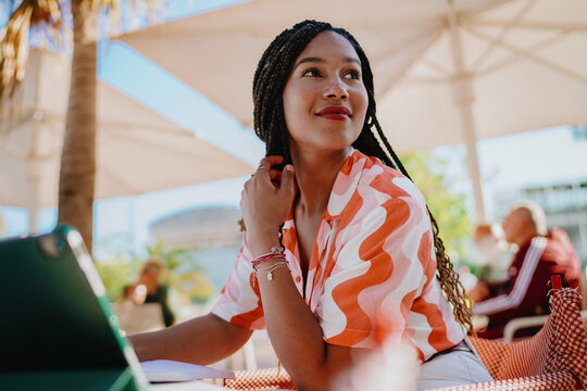 Smiling woman with braided hair sitting at table beside tablet, symbolizing confidence, optimism, and the role of mobile technology in empowering modern freelance and digital lifestyle.