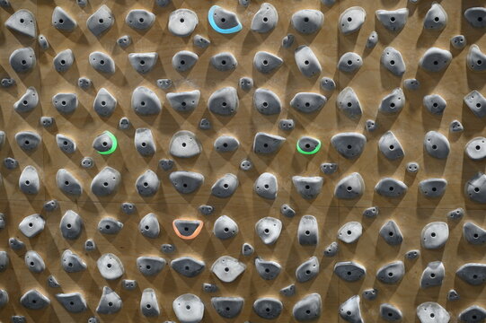 Indoor rock climbing wall (Kilter board) with colorful holds arranged on plywood surface, modern bouldering gym texture background, fitness training concept with varied grips and routes.