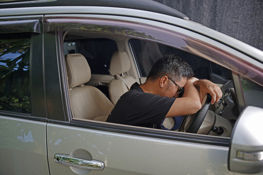 Asian male driver asleep at the wheel. Young man sitting in his car, his hands and head on the wheel. Campaign for safe driving. Working overtime