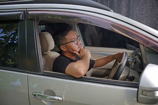 Man sits inside car, thoughtful, hand near mouth, gaze directed forward. He seems focused, perhaps waiting or contemplating. Ideal for scenes of travel, decision-making, or pause