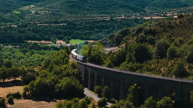 Aerial view of train crossing an ancient stone viaduct in a green mountain valley