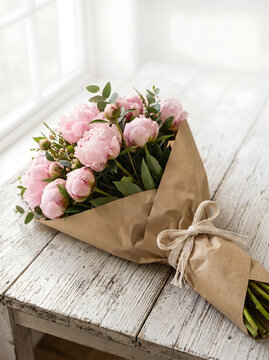 Pink peony bouquet wrapped in kraft paper on rustic wood table