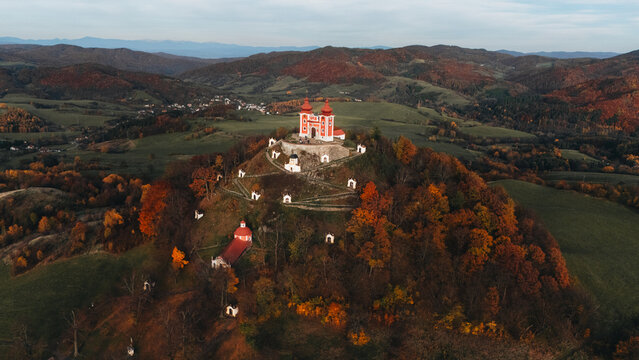 Aerial view of Kalvaria Banska Stiavnica with its red-roofed chapels on a hilltop surrounded by vibrant autumn foliage and rolling hills in Banska Stiavnica, Banskobystricky kraj, Slovakia.