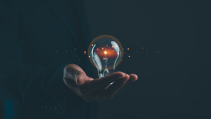 A hand holds a glowing light bulb, symbolizing ideas, innovation, and creativity against a dark background. © waragron