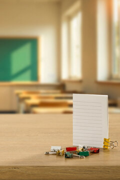 School and office items arranged on desk or classroom bench with clean copy space for product placement. Blurred classroom interior enhances the concept of education, studying and office work.