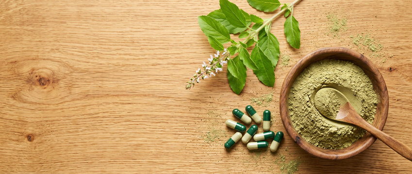 herbal medicine concept with kratom powder and capsules on wooden table with fresh leaves