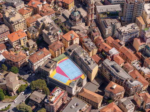 Aerial view of the colorful rooftop basketball court surrounded by historic buildings and the Basilica dei Santi Gervasio e Protasio in Rapallo, Liguria, Italy.