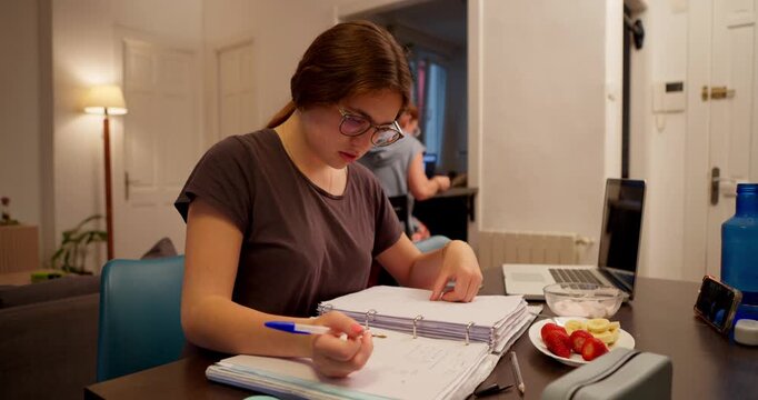 Focus and Study: A young person engrossed in studying, meticulously penning notes and pouring over written materials. The setting suggests a space dedicated to focused work and learning. 