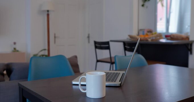 Cozy Workspace: A serene indoor setting captures the essence of a modern work-from-home setup, featuring a laptop and coffee cup arranged thoughtfully on a dark wooden table in a well-lit space.