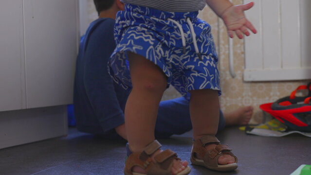 Toddler holding fruit while getting up from kitchen floor next to older brother sitting nearby, candid family moment showing playfulness and everyday life at home