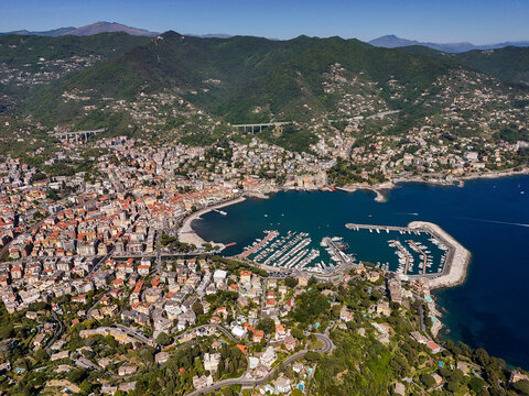Aerial view of the harbor filled with yachts, coastal buildings, and lush green hills under a clear blue sky Rapallo, Liguria, Italy.