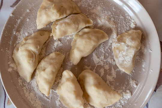 Plate of freshly prepared vareniki dumplings dusted with flour, arranged neatly on a round dish, showcasing their unique shape and texture in a home kitchen setting