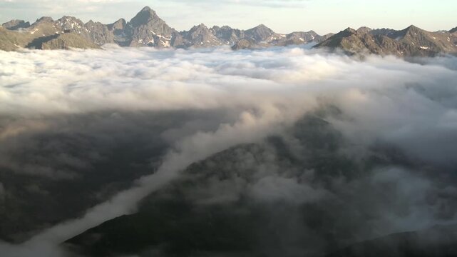 Panoramic mountain peaks rise above clouds with rugged ridges and high altitude drama. Misty layers, vapor flow, elevated relief create striking atmospheric scenery across remote ranges.