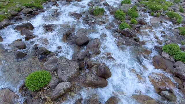 Aerial mountain stream rushes over rocks through alpine terrain with clear fast water and raw energy. Fresh current, stony channel, lively runoff shape a vivid highland creek scene for nature search.