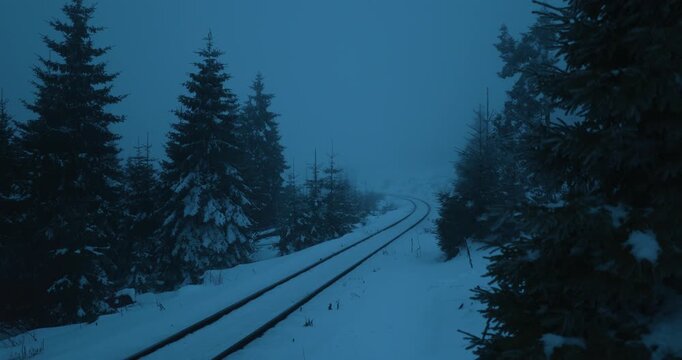 Eisenbahn f&auml;hrt bei blauer Stunde durch neblige Winterlandschaft, Frontlichter leuchten entlang verschneiter Gleise in kalter D&auml;mmerung