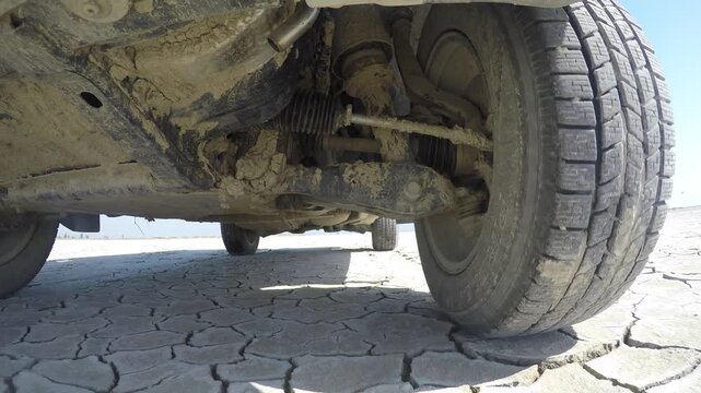 Front wheel of 4x4 SUV driving across flat desert terrain, dusty offroad motion detail. Tire action, suspension strain, rugged vehicle performance, arid ground, travel power, stock search wording.