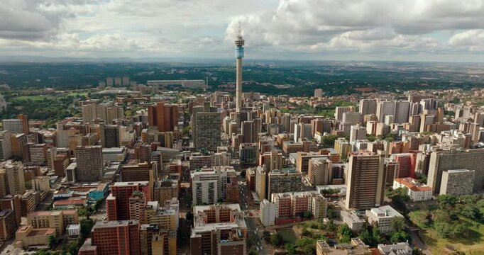 Aerial wide panning shot across Johannesburg skyline featuring Hillbrow Tower. Dramatic drone panorama of South African urban landscape, dense city architecture, and metropolitan horizon.