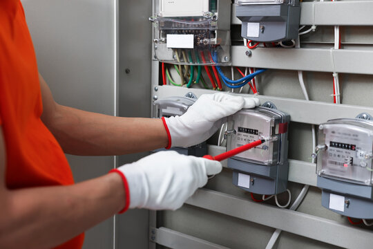 Electrician with screwdriver checking electrical meter indoors, closeup