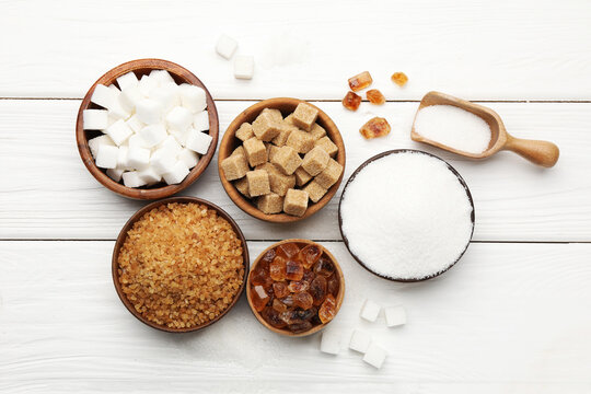 Different types of sugar on white wooden table, flat lay