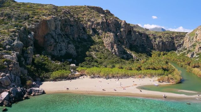 Aerial view of Preveli beach flying into narrow palm river canal, Crete, Greece. Drone forward flight from Libyan sea and rocks along tropical palm forest canyon. Exotic natural landmark, 4k video.