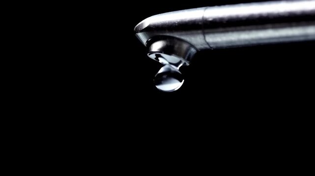 Faucet water droplet dripping slow-motion macro on black background. water droplets dripping down from a tap into a sink in the kitchen interior