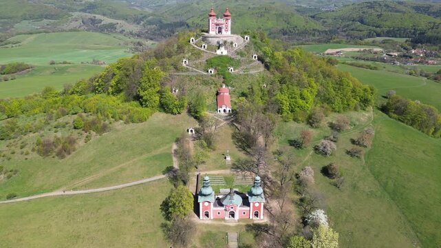 Aerial perspective of the Calvary complex in Banska Stiavnica, a baroque architectural landmark on a hill surrounded by lush green landscape