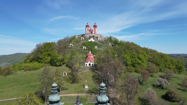 Stunning aerial perspective of the historic Calvary church complex in Banska Stiavnica, Slovakia, descending over the lush green hill