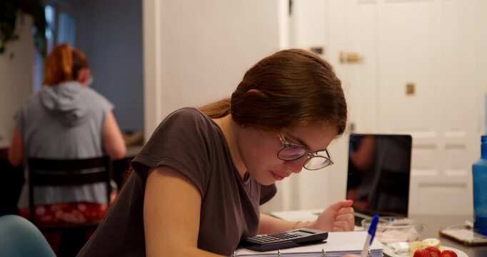 Focused Study Session: A young student, engrossed in her studies, leans over a desk with a notebook and pen, a picture of concentration and dedication.