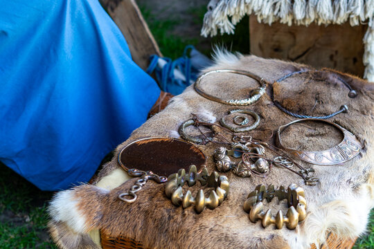 Historical bronze and brass jewelry including torcs necklaces bracelets and hand mirror displayed on natural animal fur and wicker basket in daylight outdoor setting reconstruction craft details close