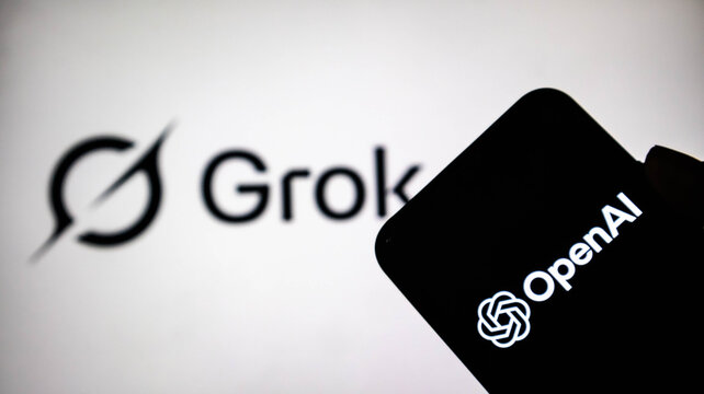 Closeup of a smartphone displaying the openai logo held in front of a screen showing the grok ai logo, representing the competition between major artificial intelligence companies