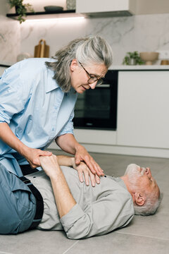 Senior woman distressed caring for ill husband on modern kitchen floor