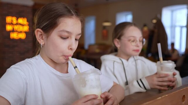 Two friends clinking milkshake glasses laughing at cafe table in festive atmosphere. Clinking, milkshake, friends, cafe, laughing.