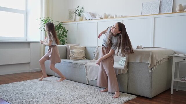 Playful teenage girls dancing barefoot on soft rug in home living room. The girls are rehearsing their contemporary performance at home.